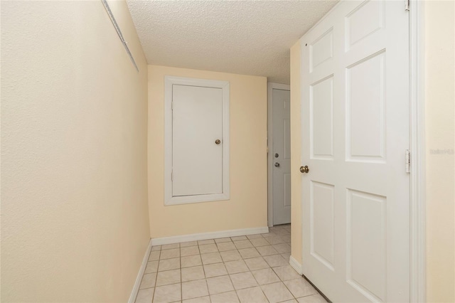 hall featuring light tile patterned floors, baseboards, and a textured ceiling