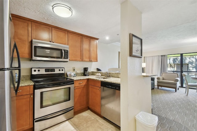 kitchen featuring appliances with stainless steel finishes, brown cabinets, a sink, and light stone counters