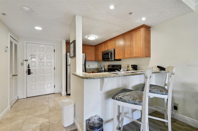 kitchen with brown cabinets, a breakfast bar area, stainless steel appliances, and a textured ceiling