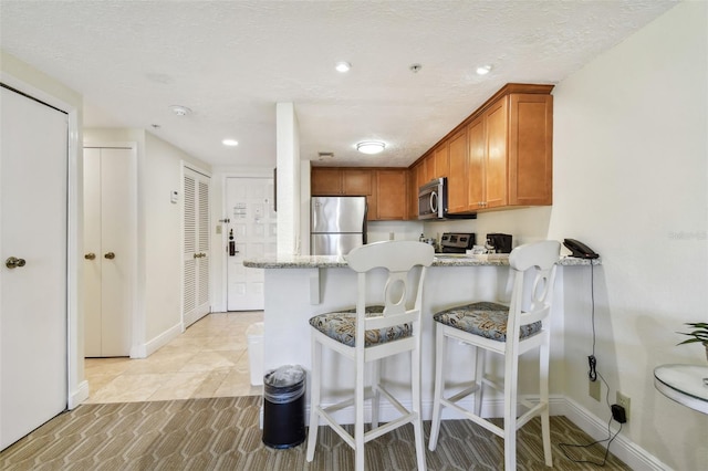 kitchen with a textured ceiling, a peninsula, appliances with stainless steel finishes, and brown cabinetry