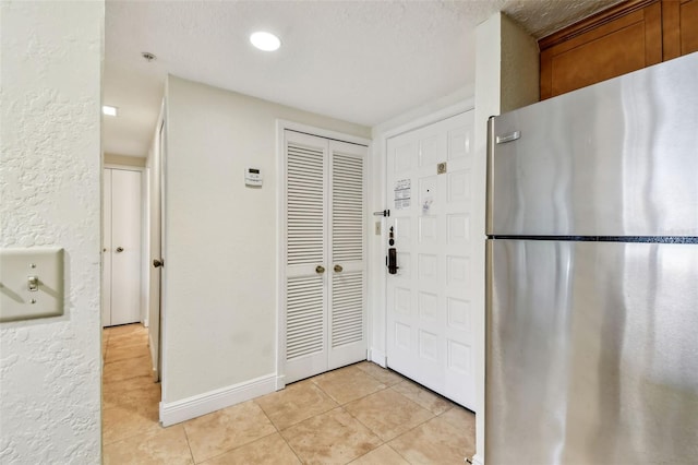 kitchen with light tile patterned floors, baseboards, a textured wall, brown cabinets, and freestanding refrigerator