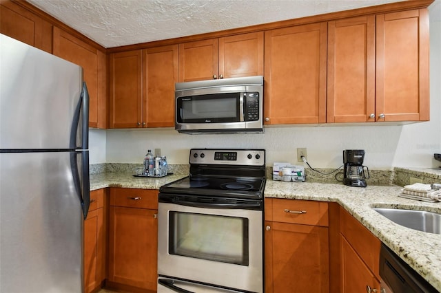 kitchen featuring light stone countertops, appliances with stainless steel finishes, brown cabinets, and a textured ceiling