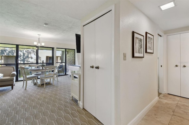 hall featuring a notable chandelier, a textured ceiling, and baseboards