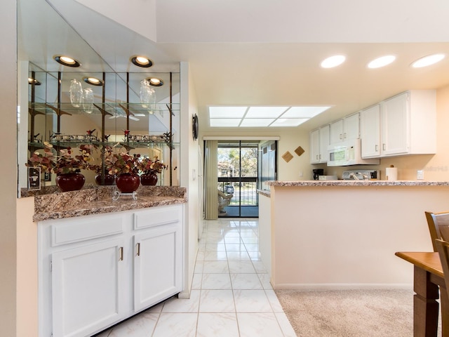 kitchen with white microwave, light stone countertops, recessed lighting, a peninsula, and white cabinetry