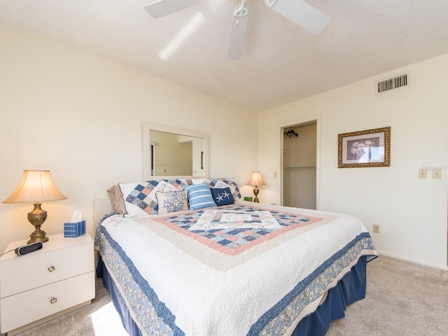 bedroom featuring visible vents, a walk in closet, a textured ceiling, light colored carpet, and ceiling fan