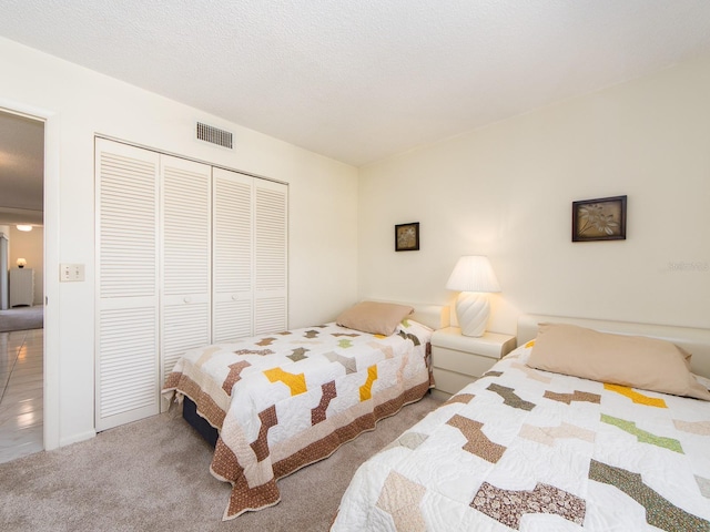 bedroom with a closet, visible vents, carpet flooring, and a textured ceiling