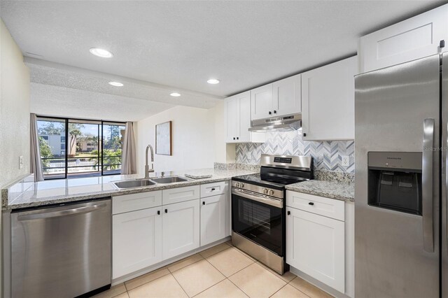kitchen with under cabinet range hood, a sink, tasteful backsplash, appliances with stainless steel finishes, and white cabinetry