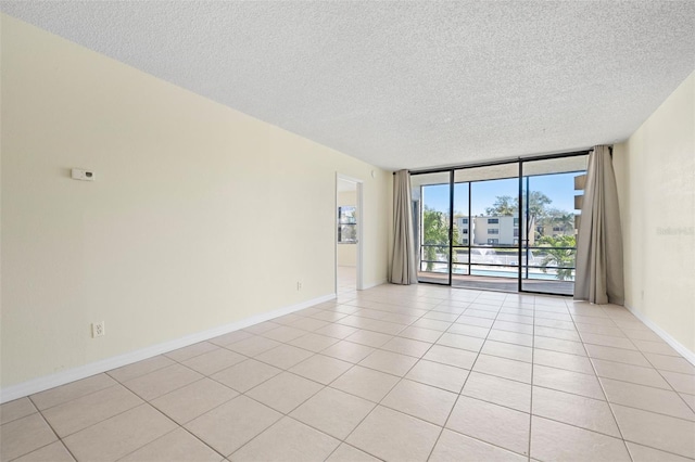 spare room featuring floor to ceiling windows, a textured ceiling, baseboards, and light tile patterned flooring