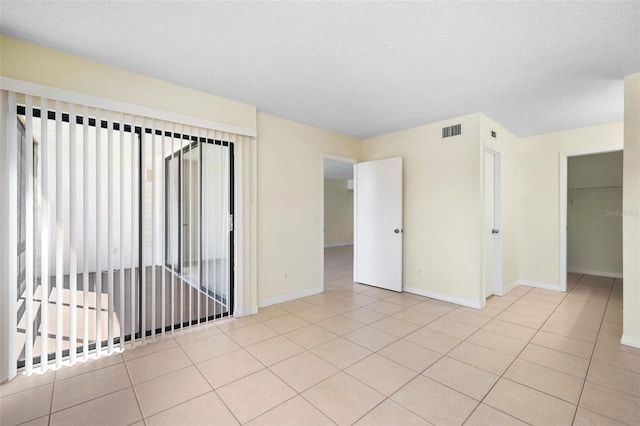 empty room with a textured ceiling, visible vents, tile patterned flooring, and baseboards