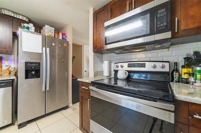 kitchen with stainless steel appliances, tasteful backsplash, light tile patterned flooring, and light stone countertops