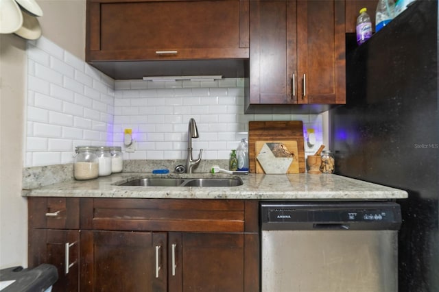 kitchen featuring backsplash, stainless steel dishwasher, freestanding refrigerator, a sink, and light stone countertops