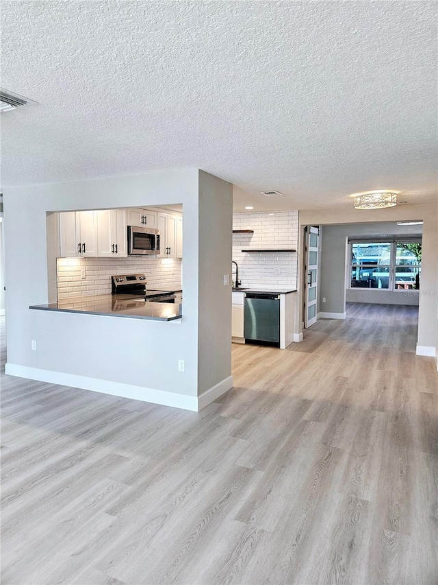 13633 Britton Dr, Hudson, FL 34667 - unfurnished living room with light wood-type flooring, a textured ceiling, visible vents, a sink, and baseboards