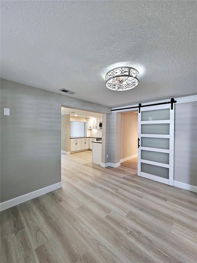 13633 Britton Dr, Hudson, FL 34667 - unfurnished living room featuring light wood finished floors, baseboards, visible vents, and a barn door