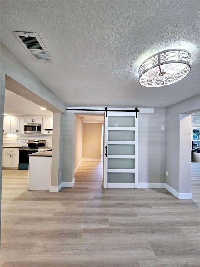 13633 Britton Dr, Hudson, FL 34667 - interior space featuring light wood-style floors, white cabinets, a barn door, visible vents, and stainless steel appliances