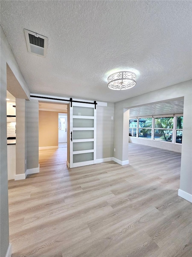 13633 Britton Dr, Hudson, FL 34667 - interior space featuring a textured ceiling, visible vents, a barn door, wood finished floors, and baseboards