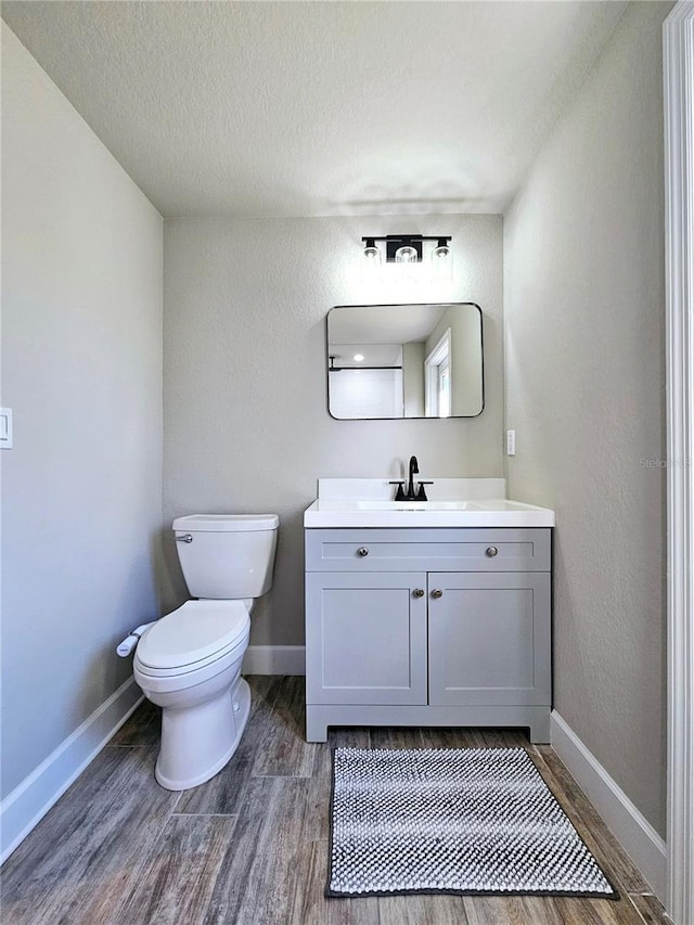 13633 Britton Dr, Hudson, FL 34667 - half bath with baseboards, toilet, a textured ceiling, vanity, and wood finished floors