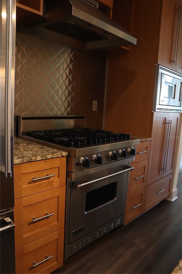 kitchen featuring dark wood-style floors, light stone countertops, stainless steel appliances, under cabinet range hood, and backsplash