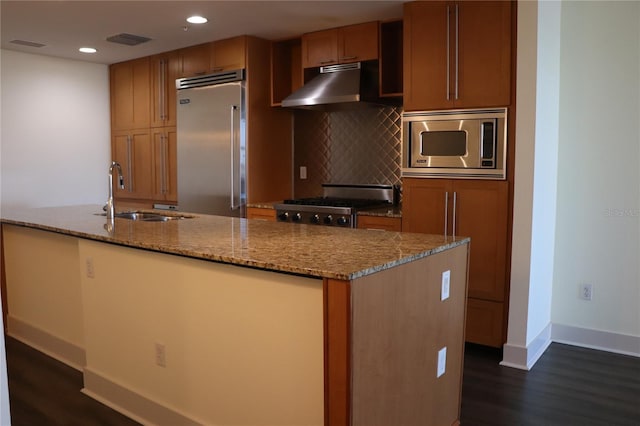 kitchen featuring backsplash, a sink, built in appliances, under cabinet range hood, and baseboards