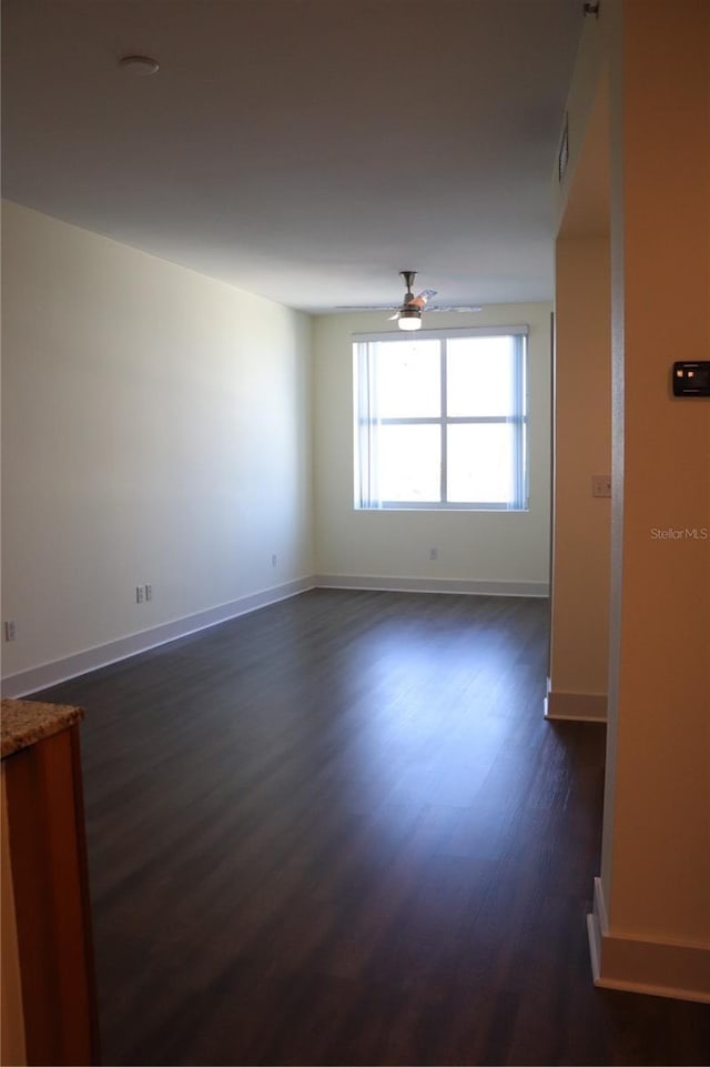 unfurnished room with ceiling fan, baseboards, and dark wood-style flooring