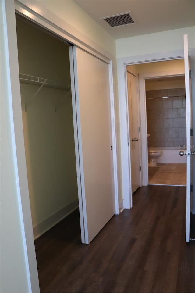 hall with dark wood finished floors, visible vents, and baseboards