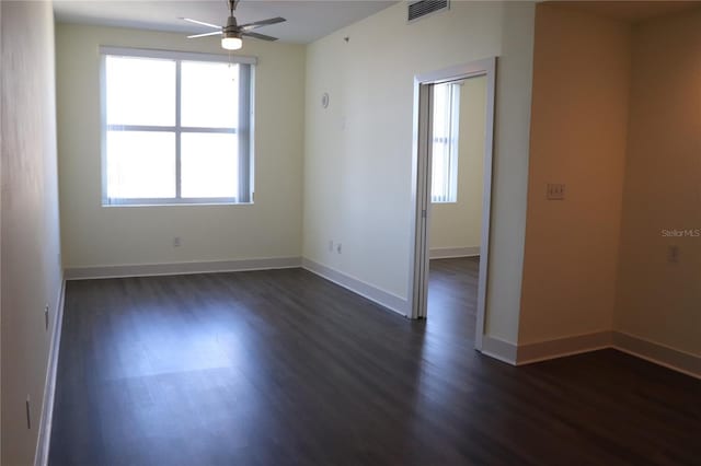 unfurnished room with baseboards, visible vents, dark wood finished floors, and a ceiling fan