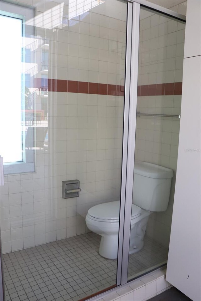 bathroom featuring a tile shower, tile patterned floors, toilet, and tile walls