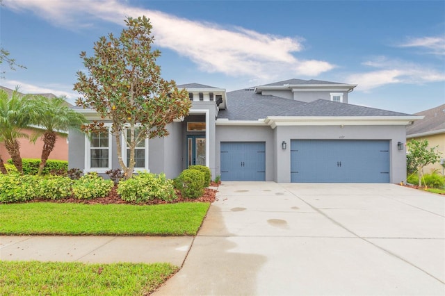 prairie-style home with stucco siding, driveway, an attached garage, and a shingled roof