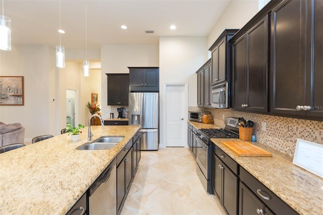 kitchen with backsplash, light stone counters, appliances with stainless steel finishes, hanging light fixtures, and a sink