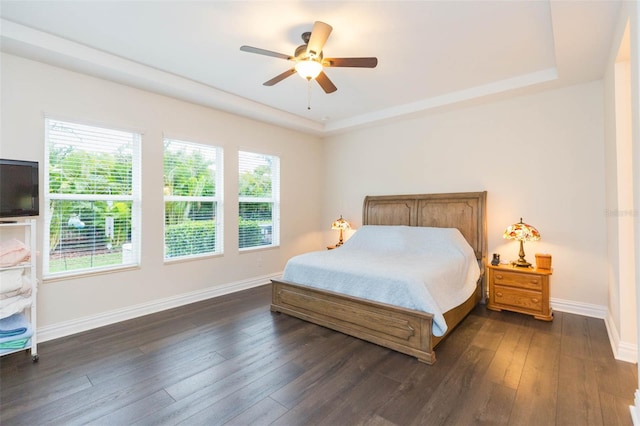 bedroom featuring baseboards, dark wood-type flooring, a tray ceiling, and a ceiling fan