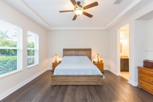 bedroom featuring baseboards, visible vents, ensuite bath, a tray ceiling, and dark wood-type flooring