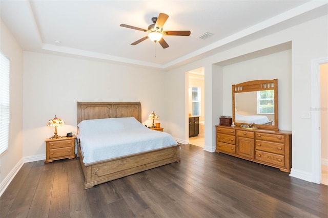 bedroom featuring visible vents, connected bathroom, baseboards, a tray ceiling, and dark wood-style floors