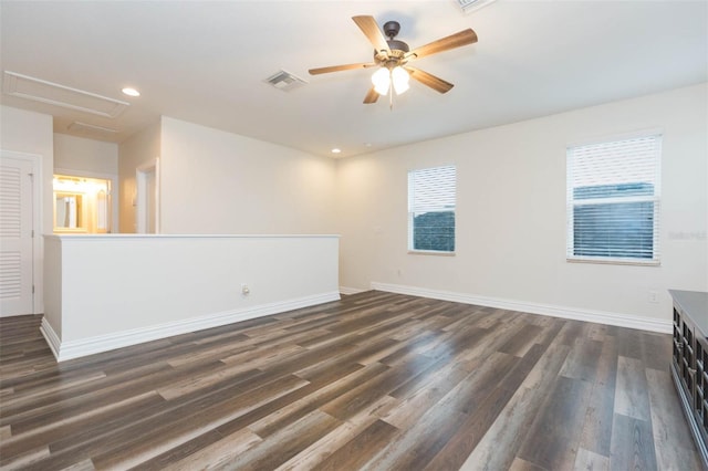 empty room featuring visible vents, a ceiling fan, dark wood finished floors, baseboards, and attic access