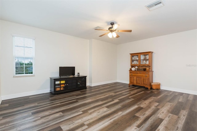 empty room featuring dark wood-style floors, a ceiling fan, visible vents, and baseboards