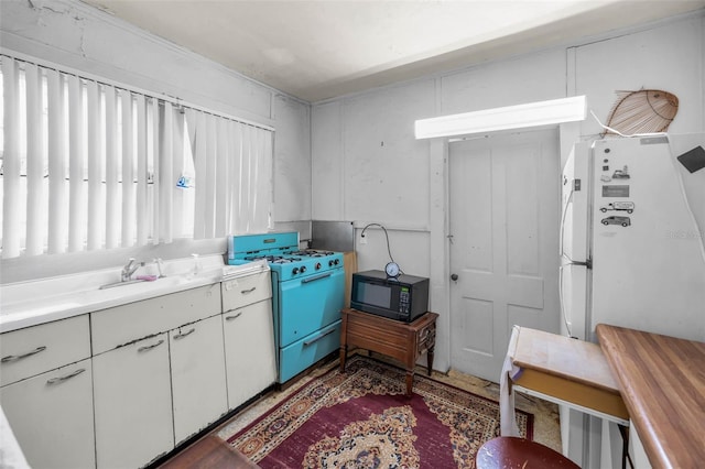 kitchen featuring gas stove, freestanding refrigerator, light countertops, black microwave, and white cabinetry