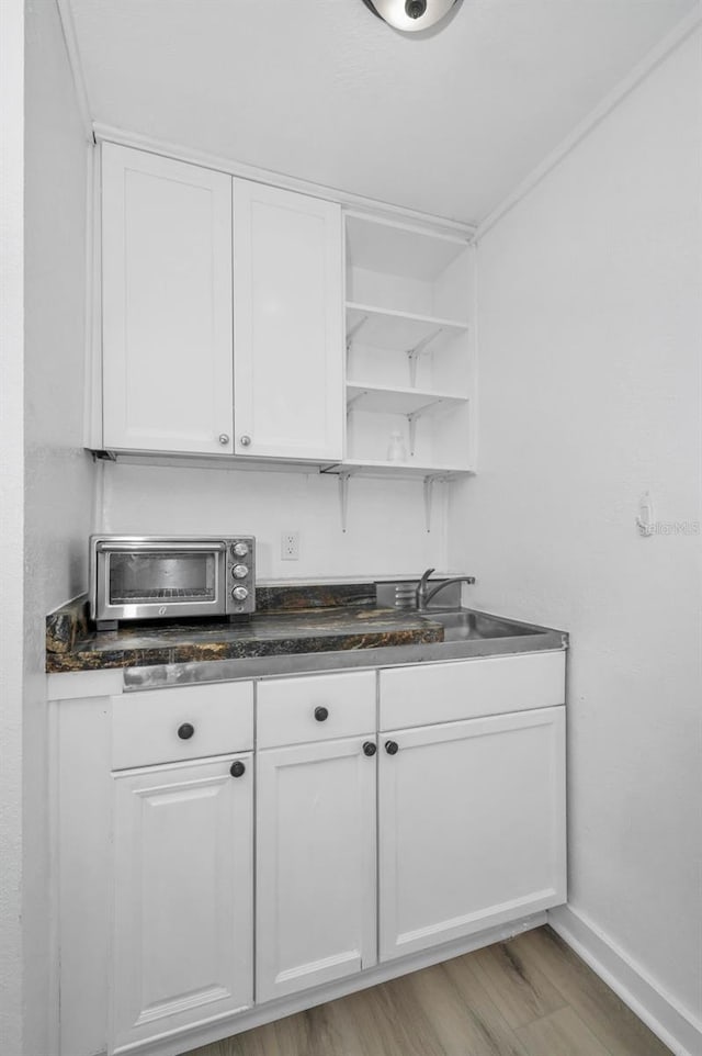 kitchen featuring light wood finished floors, open shelves, a toaster, white cabinets, and a sink