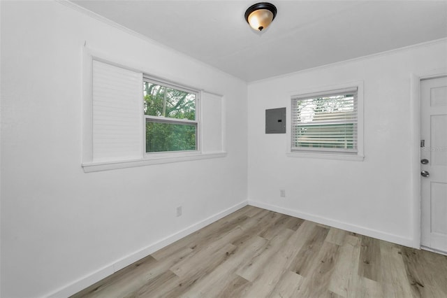 empty room featuring electric panel, baseboards, light wood-style flooring, and crown molding