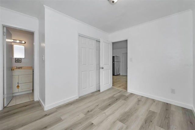 unfurnished bedroom featuring light wood finished floors, a closet, freestanding refrigerator, and ornamental molding