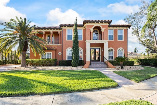 mediterranean / spanish-style home featuring a balcony, stucco siding, a front yard, and french doors