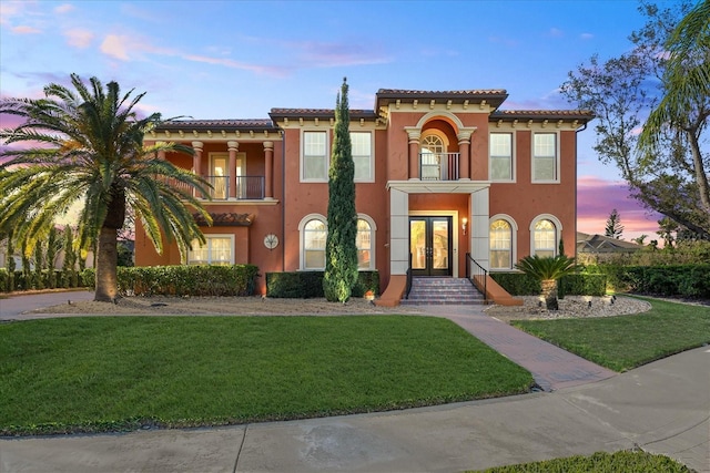 mediterranean / spanish-style house featuring french doors, a front lawn, a balcony, and stucco siding