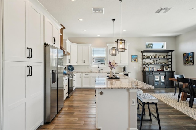 kitchen featuring dark wood-type flooring, a sink, a center island, appliances with stainless steel finishes, and a breakfast bar area