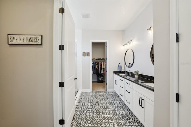 full bath with double vanity, baseboards, a spacious closet, and a sink