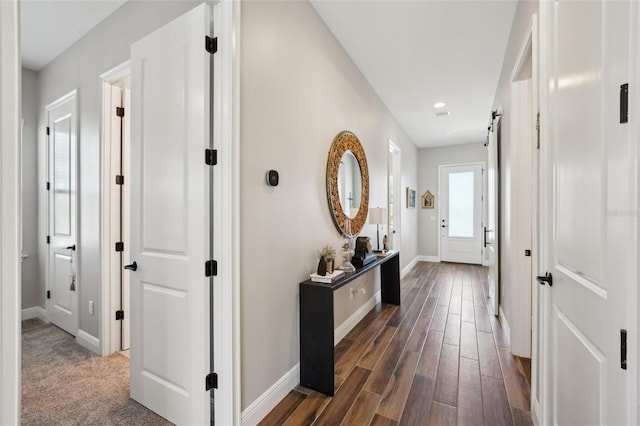 hall with dark wood finished floors, a barn door, recessed lighting, and baseboards