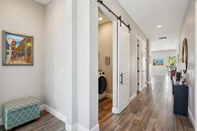 corridor featuring wood finish floors, visible vents, a barn door, baseboards, and washer / dryer