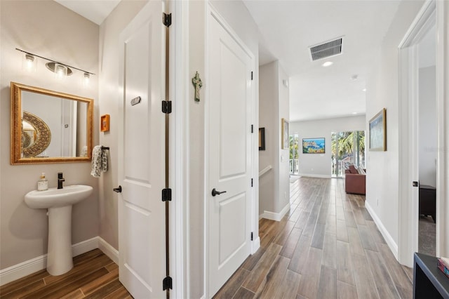 corridor with baseboards, visible vents, wood finish floors, recessed lighting, and a sink