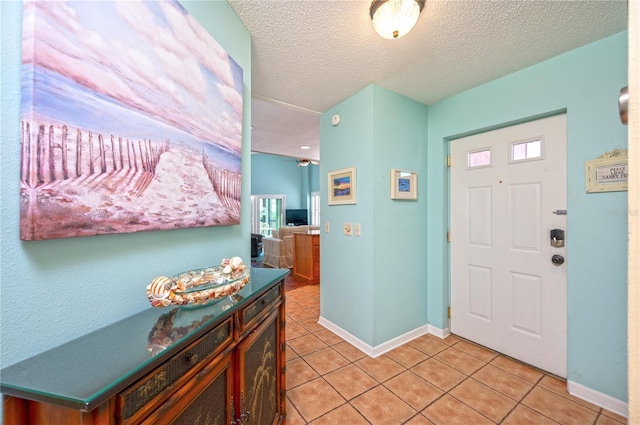 entryway featuring light tile patterned flooring, a textured ceiling, baseboards, and a ceiling fan