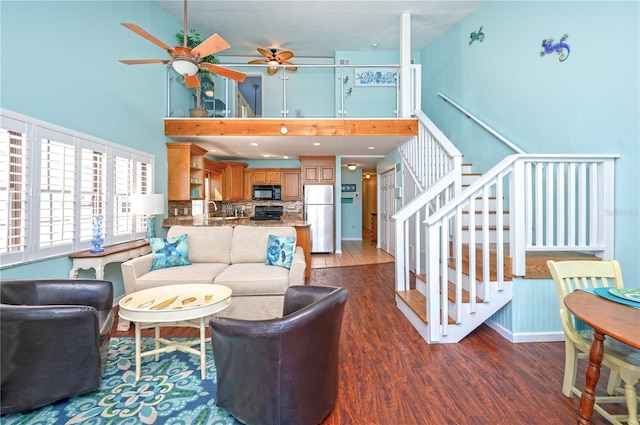 living room featuring a ceiling fan, stairs, a towering ceiling, and wood finished floors