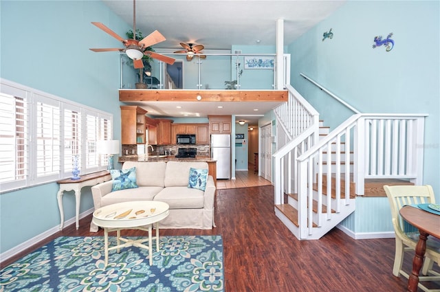 living room featuring a ceiling fan, wood finished floors, stairway, baseboards, and a towering ceiling