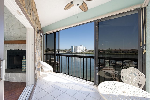 sunroom / solarium featuring a stone fireplace, ceiling fan, and a water view