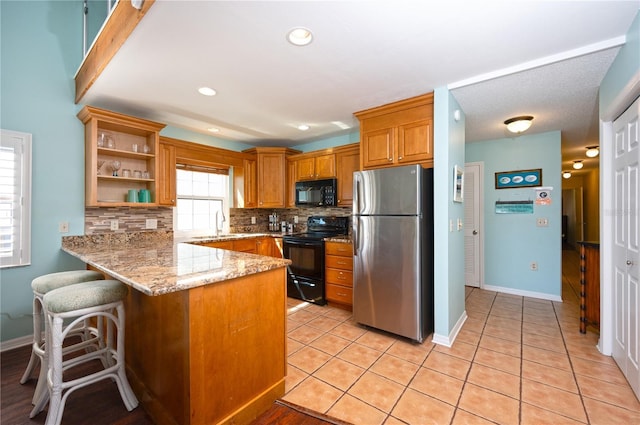 kitchen with light stone countertops, a peninsula, open shelves, decorative backsplash, and black appliances