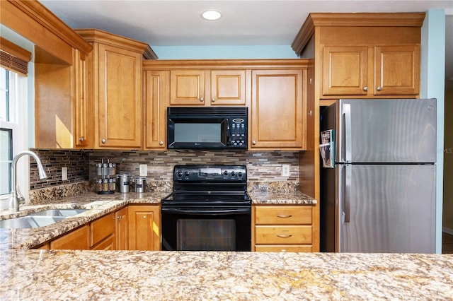 kitchen featuring decorative backsplash, black appliances, light stone countertops, and a sink